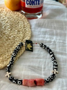 Bracelet with decorative beads on a white surface, with a hat and glass in the background.